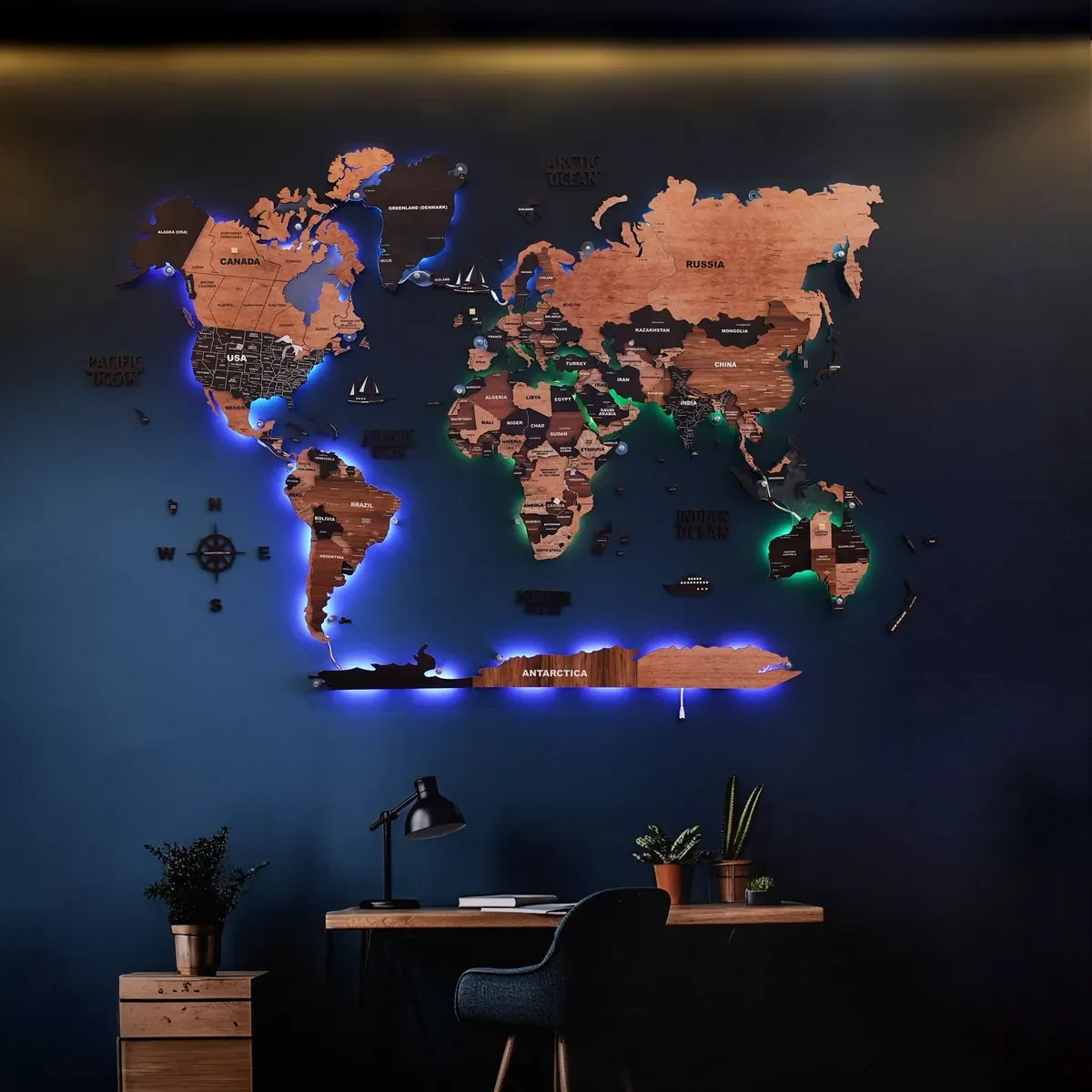 Warm wooden world map with blue and green LED backlighting on a dark wall above a desk